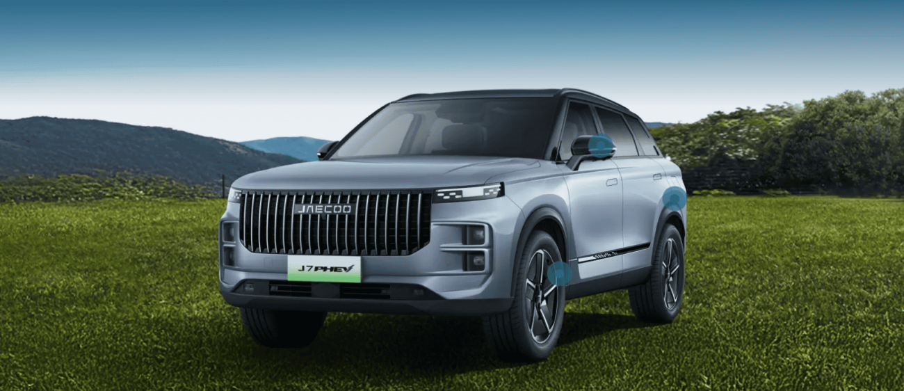 Jaecoo J7 PHEV car in moonlight silver on a green field with hills in the background.