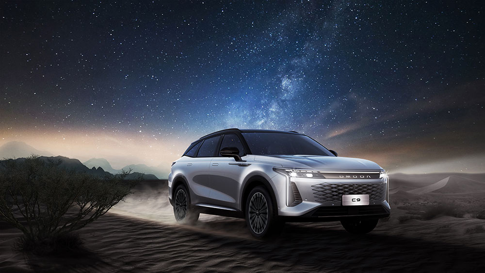 Omoda C9 SUV in matte grey driving on desert sand under a starry night sky.